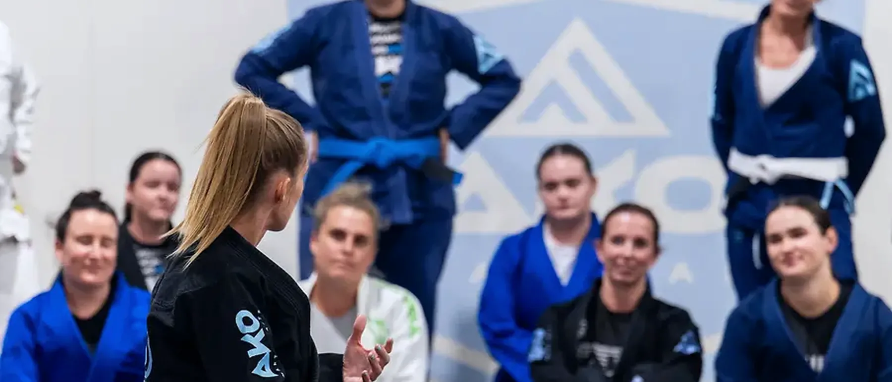 A women's class listening to a coach on the mats at Ako Martial Arts
