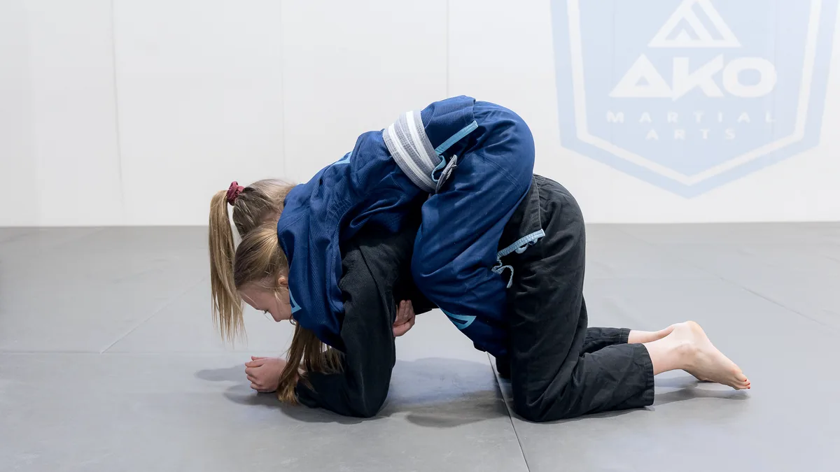 A young girl turtled up on the mats, still working, during a junior class at Ako Martial Arts