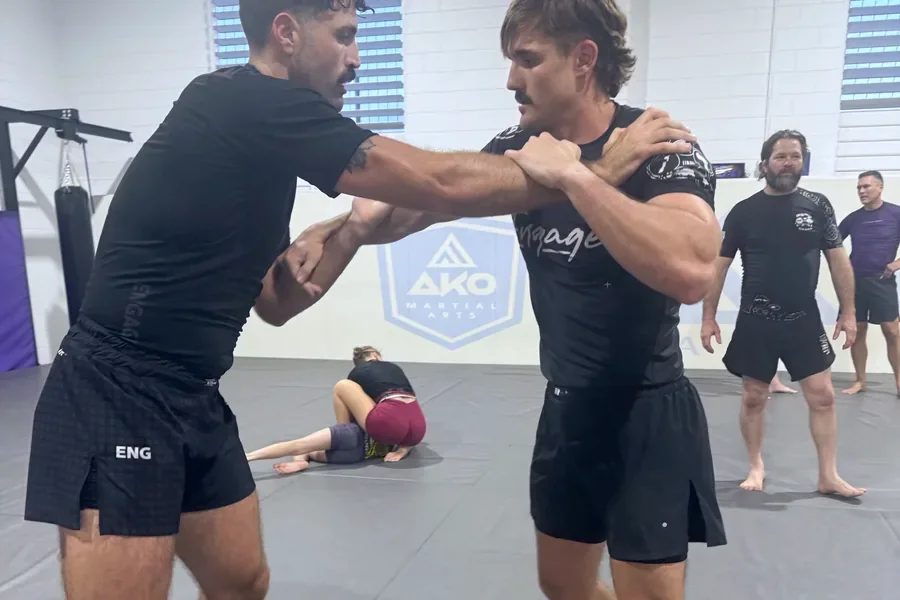 Two adults working a clinch during an MMA class at Ako Martial Arts, with the rest of the class training behind them